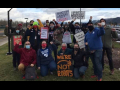 A group of Amazon solidarity activists pose for a photo with their fist raised. Some hold signs that read "Put Workers First," "Amazon Workers Need a Union," and "Solidarity Forever."