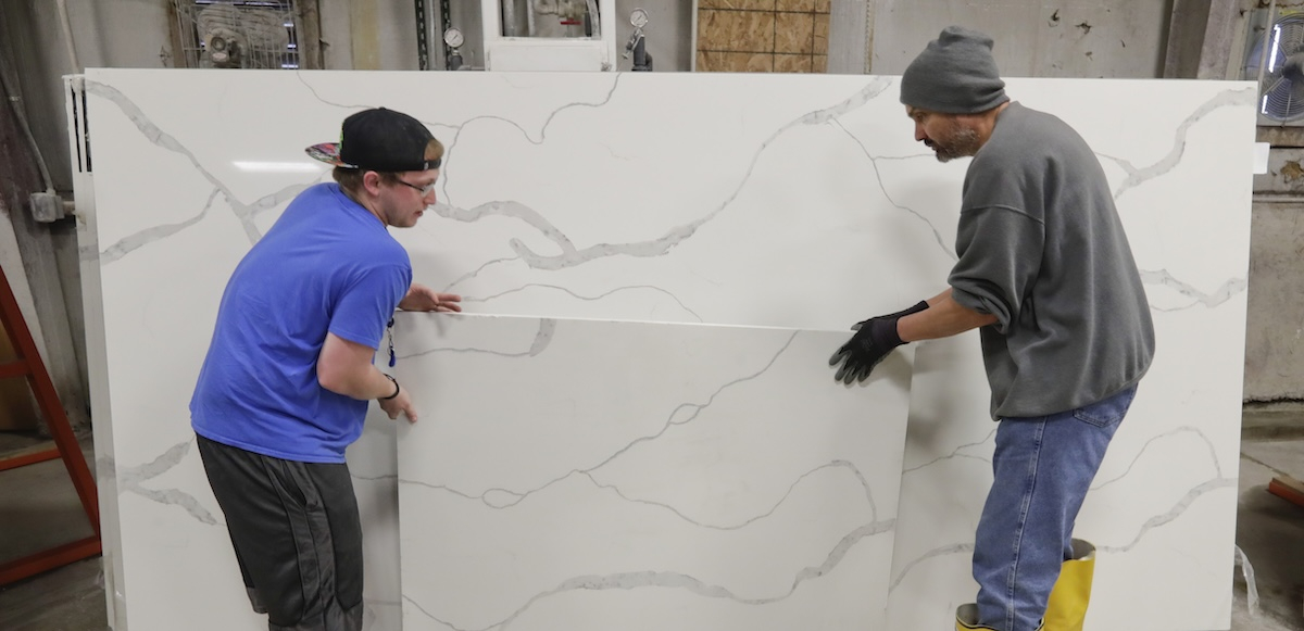 Two workers place a slab of manufactured stone against a larger slab.