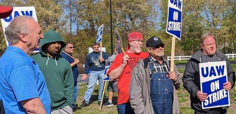 A group of workers looks to the left, with signs saying UAW on strike