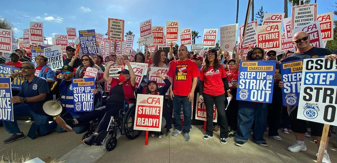 A crowd of 80 stands looking at the camera with red and white signs saying “CFA Strike Ready” 