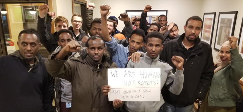 Amazon workers with fists raised gathered around a sign.