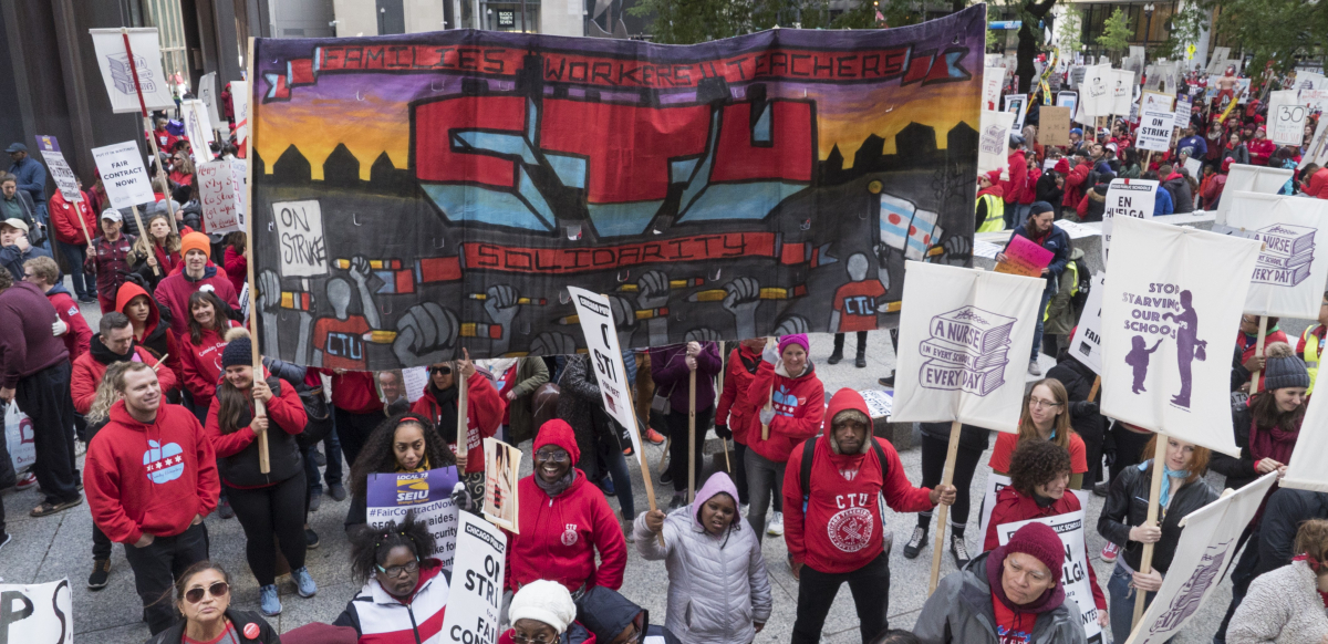 Dozens of strikers stand around a Chicago Teachers Union banner.