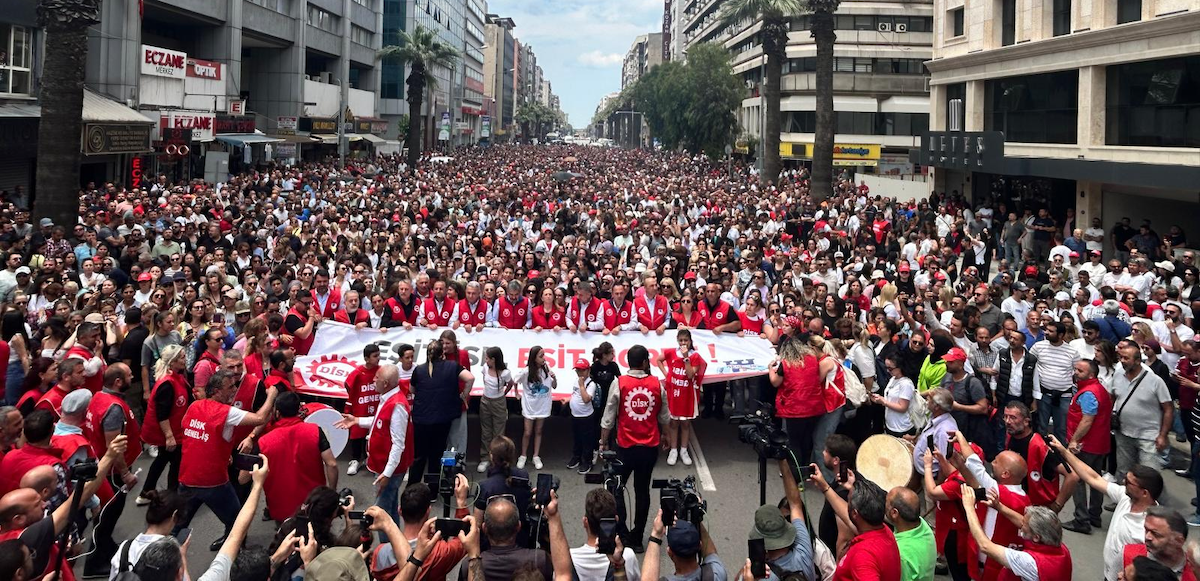 A huge crowd, as far as the eye can see, many wearking red, march down a street flanked by tall buildings.