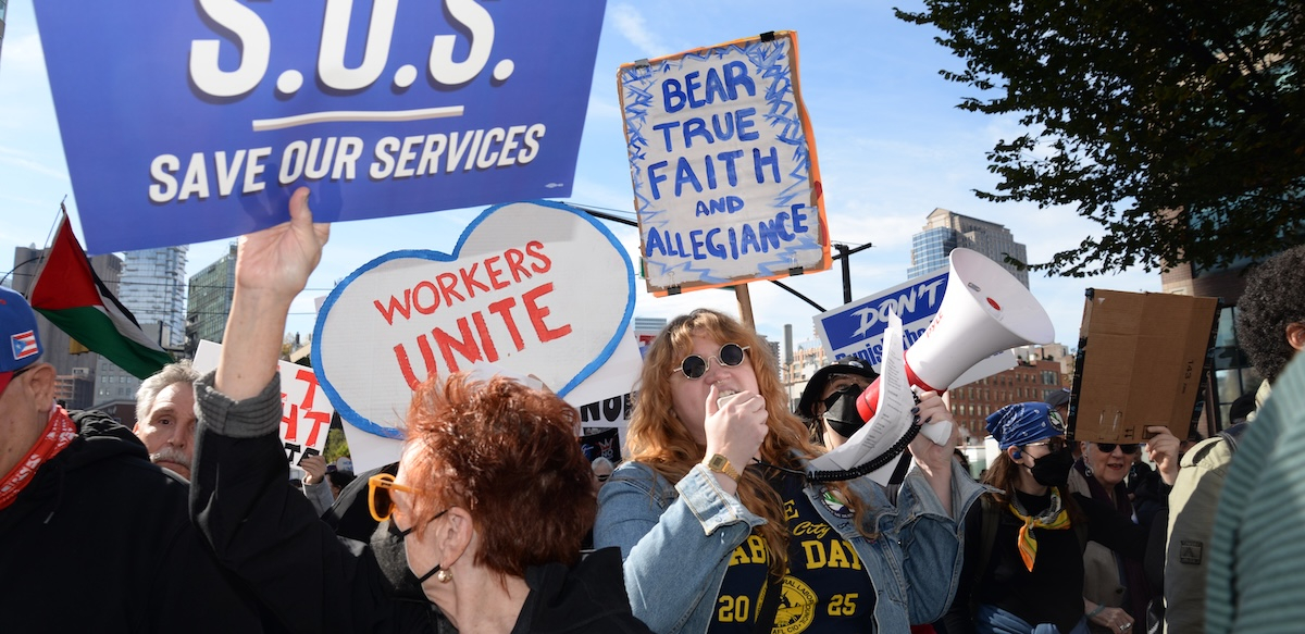 A close crowd with signs, including ‘Save our Services’ and someone with a bullhorn
