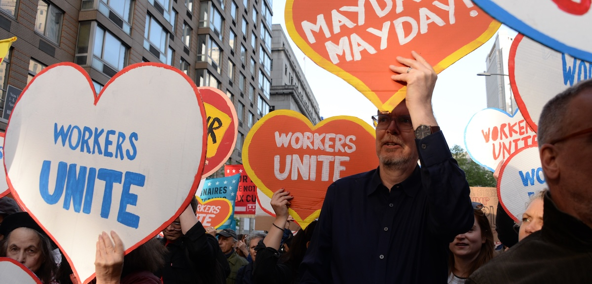 People march with heart-shaped signs saying “workers unite” and “May Day!”