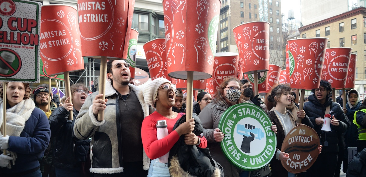A crowd raise huge red cups that say “Baristas on Strike”