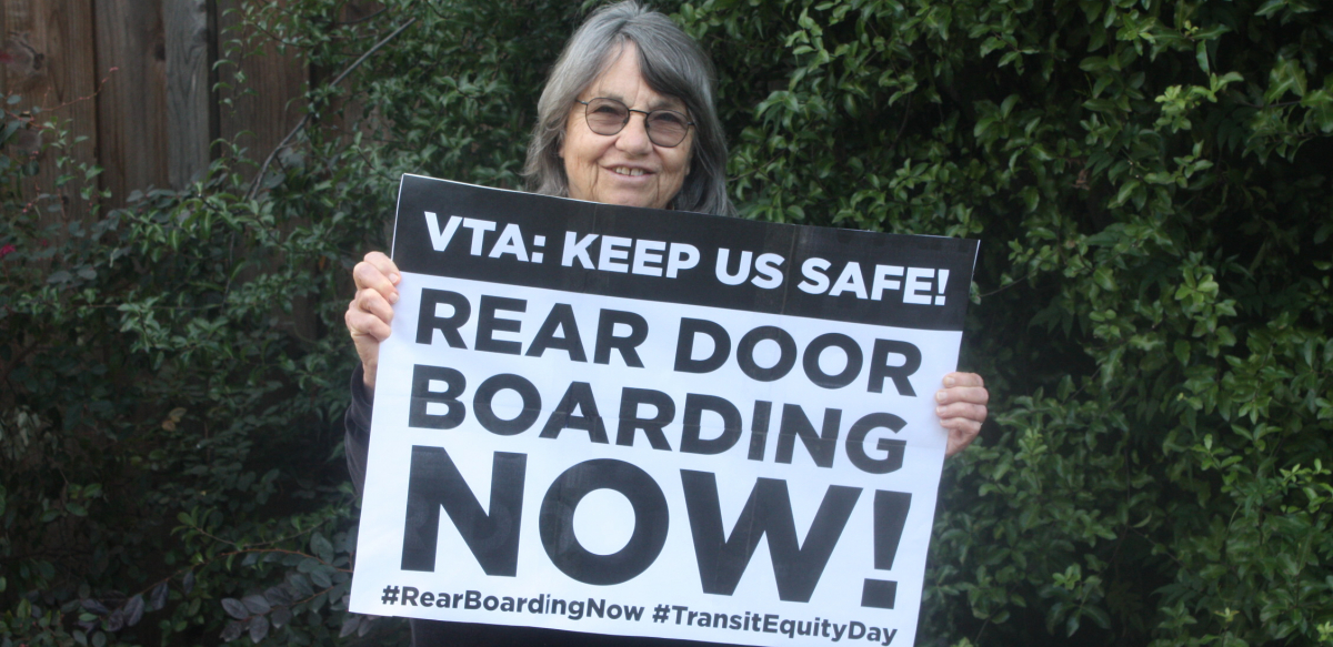 Woman holds sign reading "VTA: Keep Us Safe! Rear Door Boarding Now! #RearBoardingNow #TransitEquityDay"
