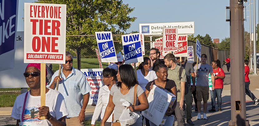 Group of UAW strkers picketing with signs against tiered wages.