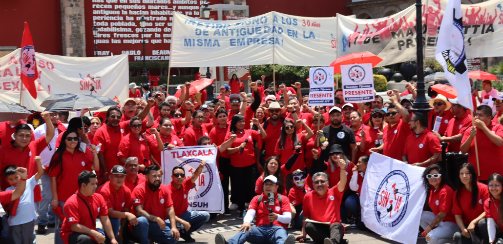 A large crowd of SINTTIA members in red shirts hold banners celebrating May Day