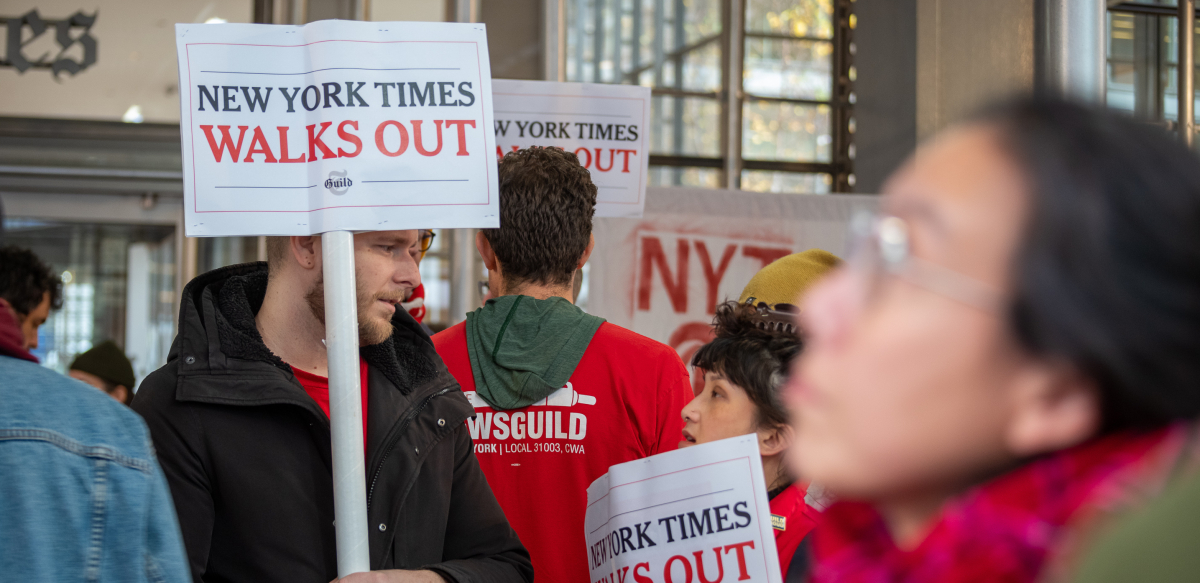 NYT Strike picketers outside New York Times headquarters with a jumble of NewsGuild signs.