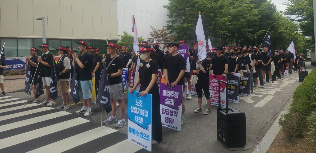 Hundreds of workers in black shirts and red headbands stand in rows of six, holding signs and flags.