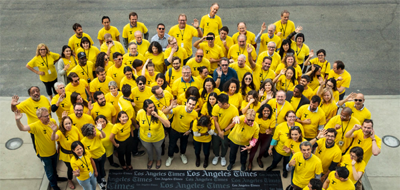 L.A. Times employees gather as NewsGuild members wearing bright yellow shirts around a plaque that says LA Times.