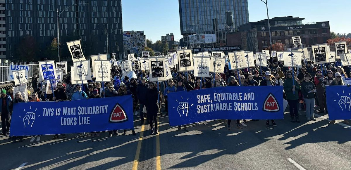 A large crowd in blue marches with banners. One says, “Safe, equitable and sustainable schools” and many carry “ready to strike” signs.