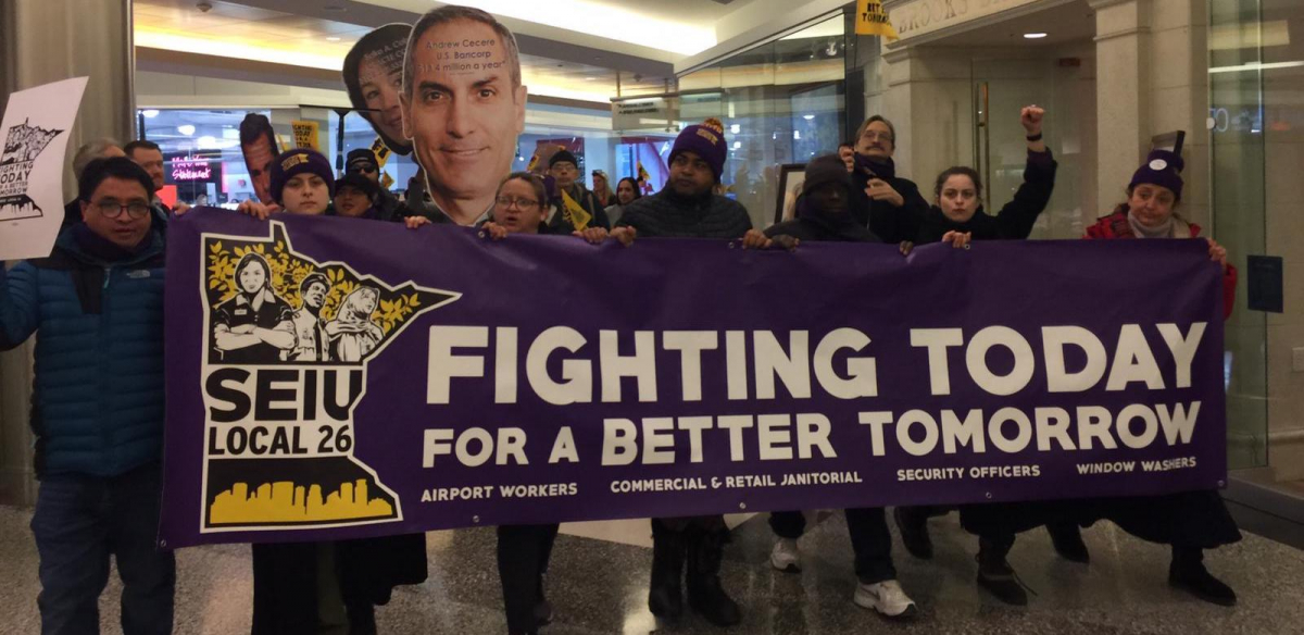 Commercial office janitors, retail janitors, security officers, window cleaners, and airport workers march through the downtown Minneapolis skyway, carrying a banner that reads "Fighting Today for a Better Tomorrow," as part of SEIU Local 26's contract campaign.