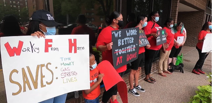 A woman holds a sign about Work from Home, while a child and a group behind her hold other signs.