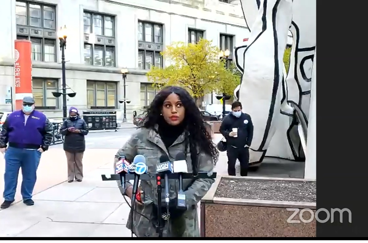 Outdoors, Stacey Davis Gates speaks at a podium with microphones; representatives of several other unions stand behind her, distanced apart