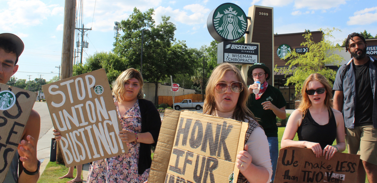 Striking Starbucks workers and supporters hold signs reading Stop Union Busting outside a store.