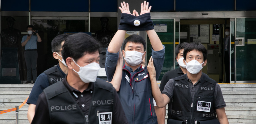 Man in mask raises handcuffed hands in air, escorted by several other masked men whose jackets read "POLICE"