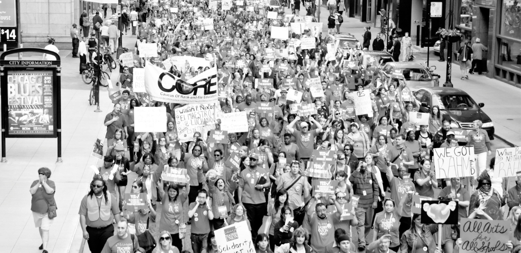 Black-and-white photo of huge crowd of Chicago teachers marching through a downtown street. Many carry signs. One large banner says "CORE," which stands for the Caucus of Rank-and-File Educators.