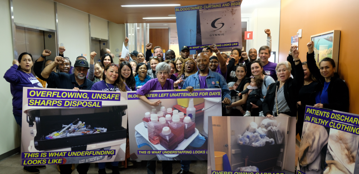 Big crowd of members in a hallway, many fists in air. Front row holds oversized photo signs with captions: "OVERFLOWING, UNSAFE SHARPS DISPOSAL: THIS IS WHAT UNDERFUNDING LOOKS LIKE." "BLO{***}ATER LEFT UNATTENDED FOR DAYS: THIS IS WHAT UNDERSTAFFING LOOKS LIKE." "PATIENTS DISCHARGED IN FILTHY CLOTHING."]