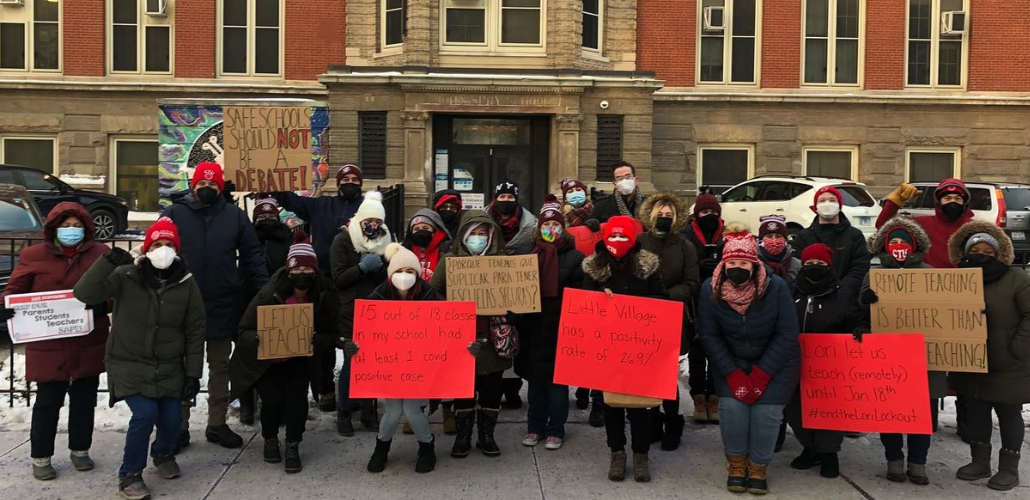 25 people in front of a school, masked and bundled up. Handmade signs read: "Keep our parents, teachers, students safe!""Safe schools should not be a debate!" "Let us teach!" "15 out of 18 classes in my school had at least 1 covid positive case" "Porque tenemos que suplicar para tener escuelas seguras?" (in Spanish: Why do we have to beg to have safe schools?) "Little Village has a positivity rate of 26.9%" "Lori let us teach (remotely) until Jan. 18th #EndTheLoriLockout"