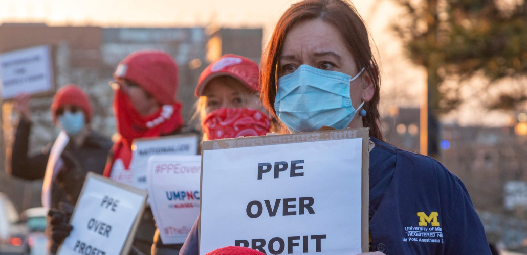 Masked workers in University of Michigan RN stand outside at dusk or dawn carrying home-printed signs: "PPE OVER PROFIT"
