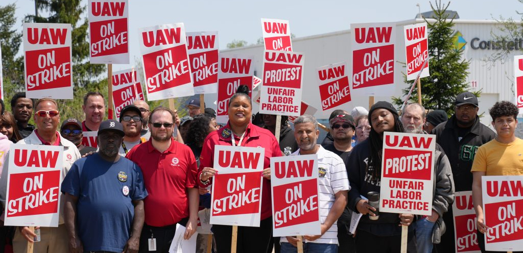 A group of workers and supporters stand holding signs reading UAW on Strike.