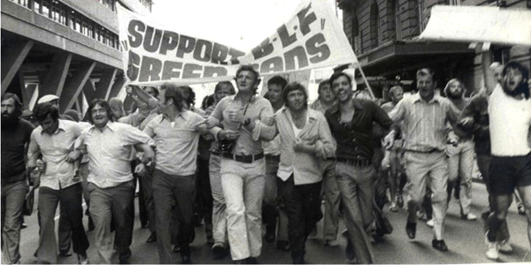 Black and white photo of men marching with a banner: "SUPPORT BLF GREEN BANS"