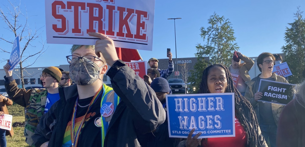 St. Louis Black Friday strike Amazon strikes hold signs saying strike, higher wages, stop racism. An Amazon facility is in the background