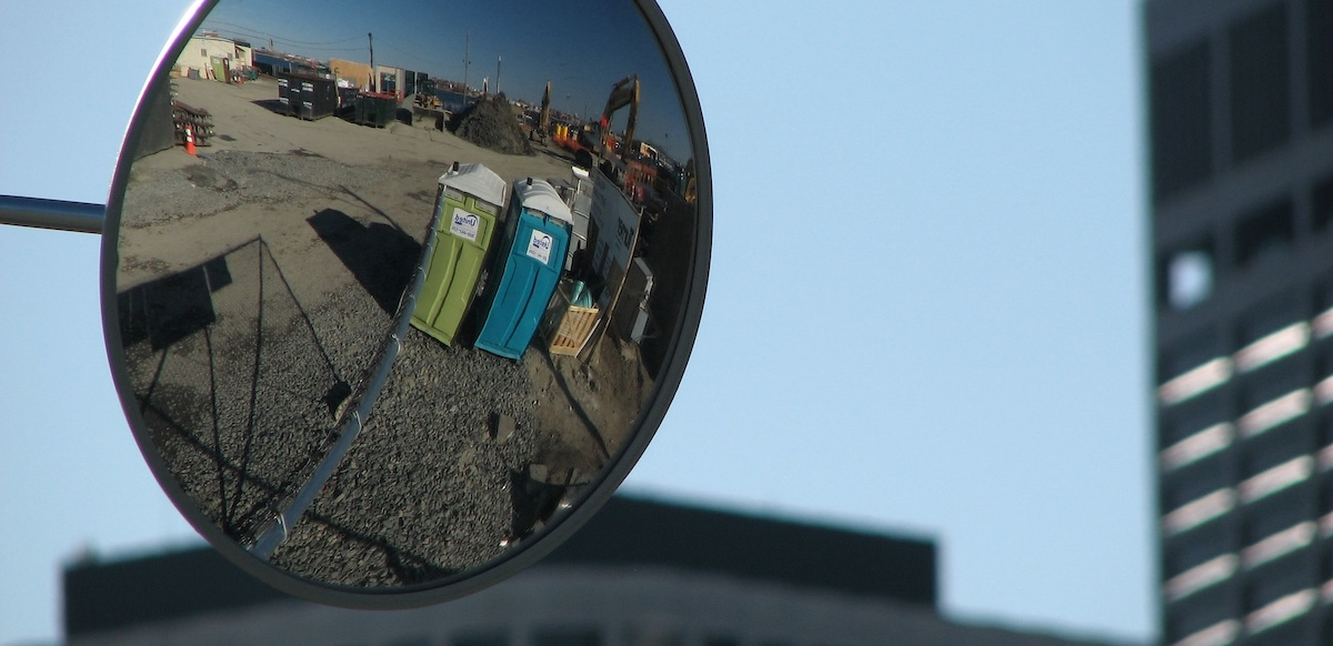 Two portajohns are reflected in a truck side mirror.