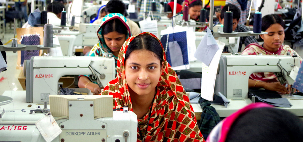 Bangladeshi garment worker at sewing machine looks up, sitting in factory