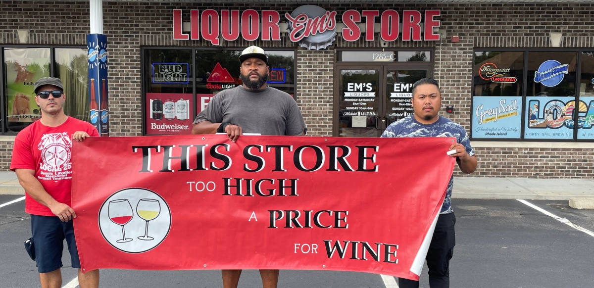 Three workers stand in front of a liquor store holding a banner that reads "This Store Too High a Price for Liquor"