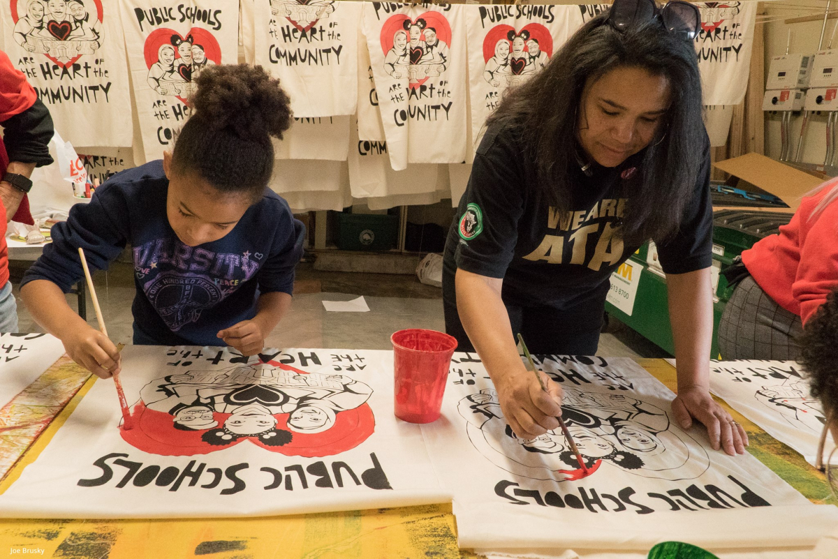 Two people painting signs that say "public schools are the heart of the community"