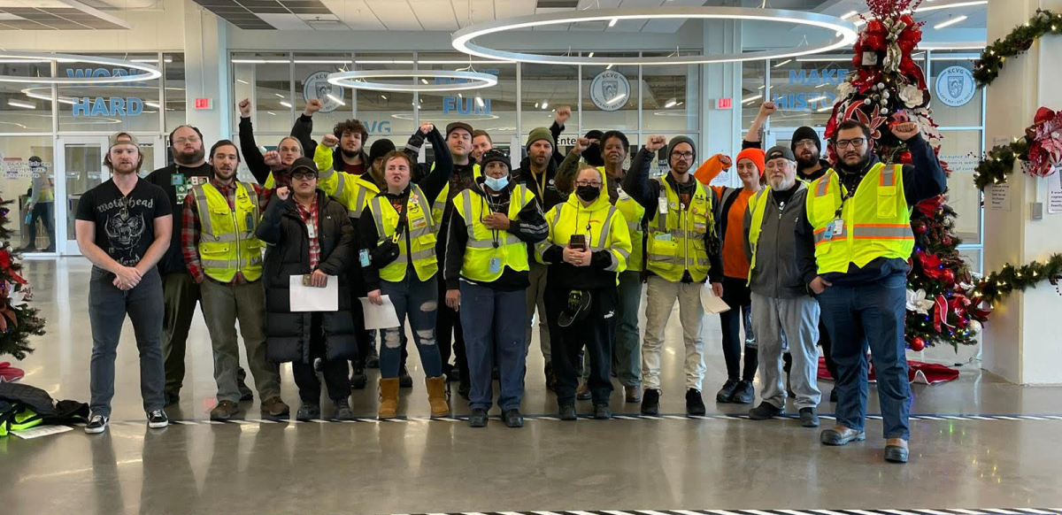 A group of Amazon workers wearing yellow hi-vis vests stands together after marching on their boss.