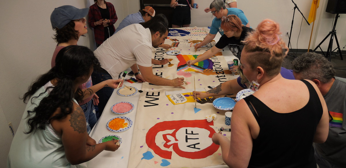 Several people work around a table adding colorful paints to a banner. Photo: ATF
