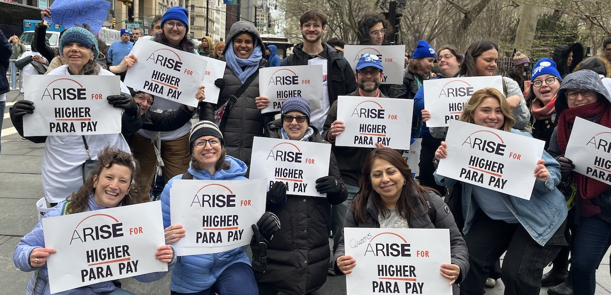 About 15 smiling people hold identical signs saying “ARISE for Higher Para Pay”