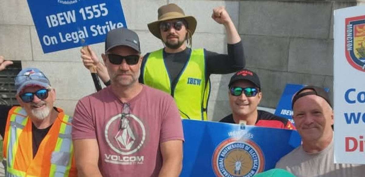 Five men in hats, sunglasses and hi-viz vests hold signs--including one that says IBEW 1555 On Legal Strike