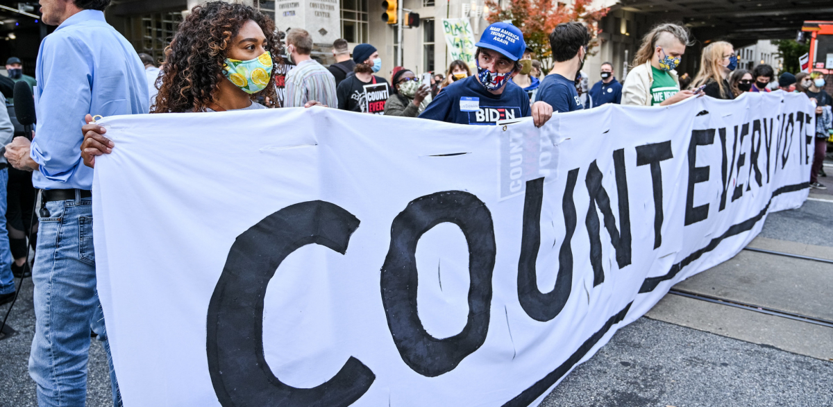 A group of people holds a large white banner with the slogan Count Every Vote.