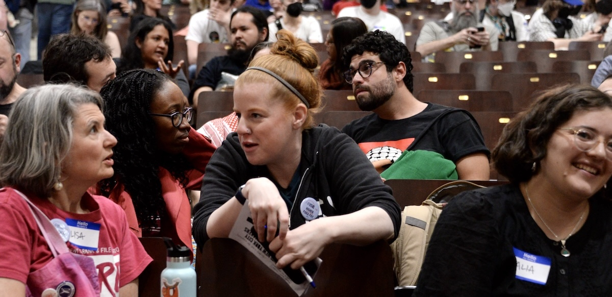 Two women talk across seats in filled auditorium.