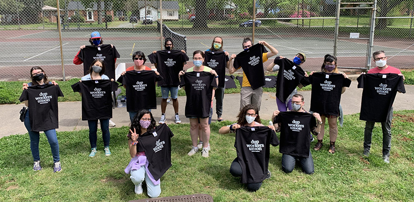 Duke University Press Workers Union posing in matching black T-shirts on grass.