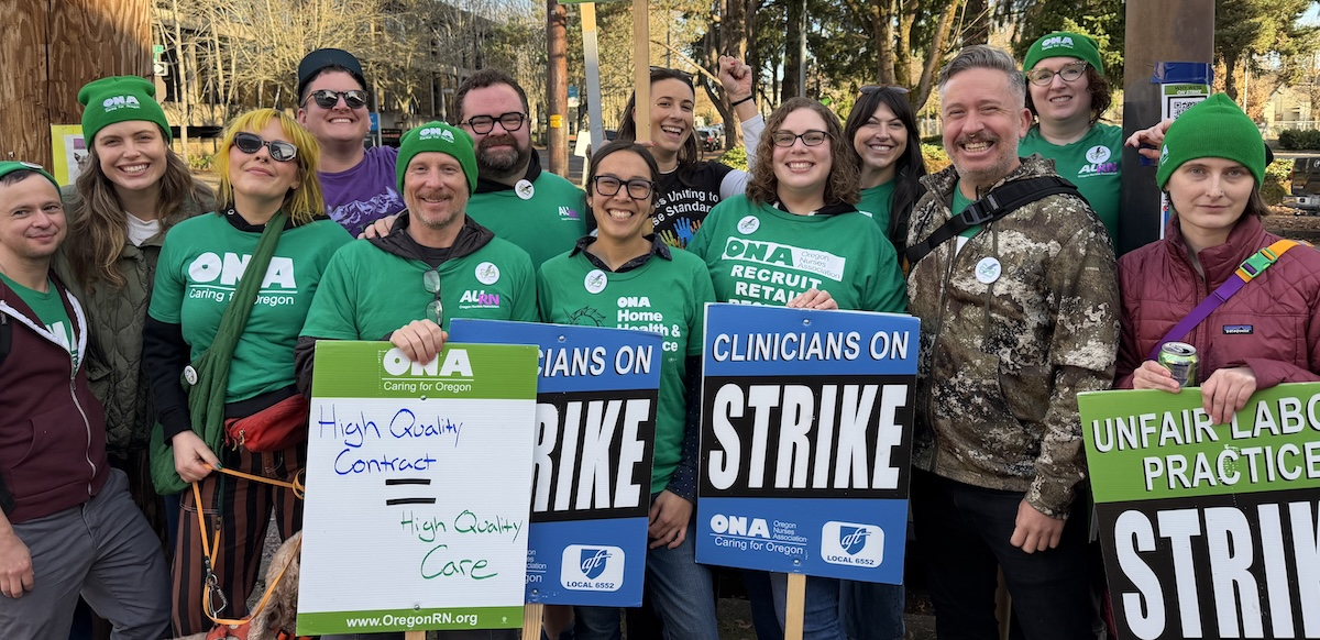 A group of green-shirted union members hold strike signs and smile.