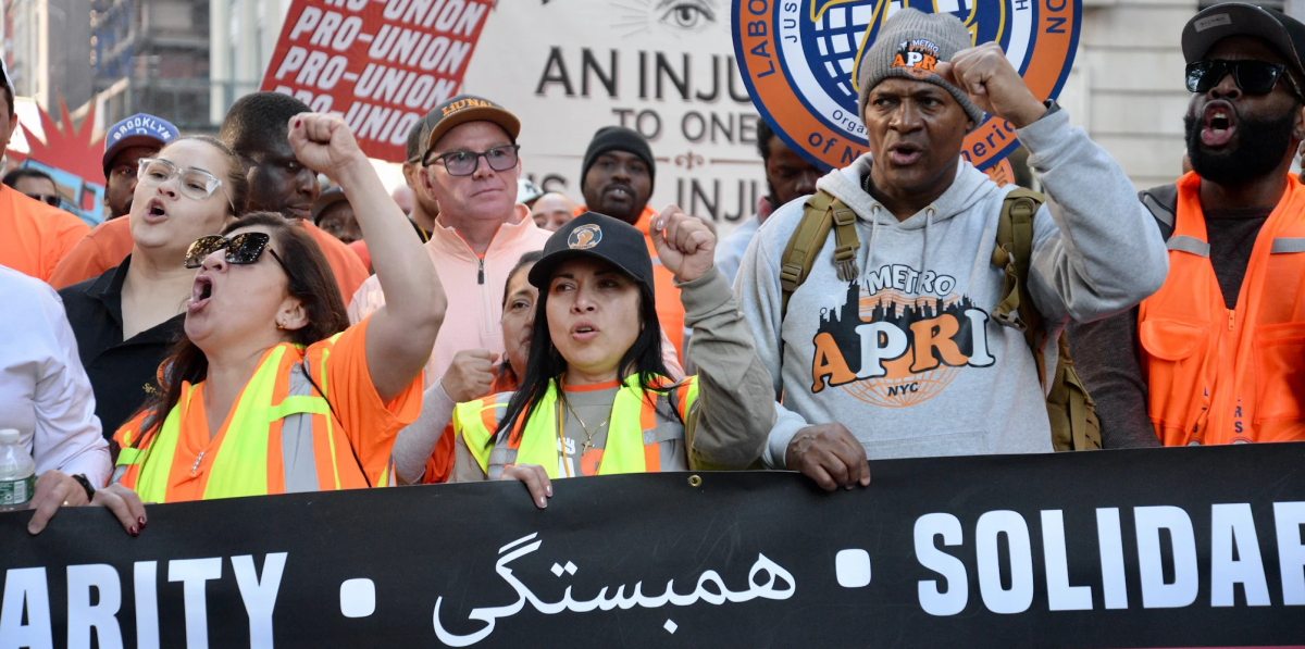 Members of the Laborers Union march during the May Day rally in New York City, behind a black banner that says solidarity in multiple languages, including Arabic.
