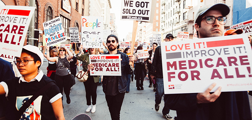 Protest in 2017 with signs that support Medicare for All, people marching in the street