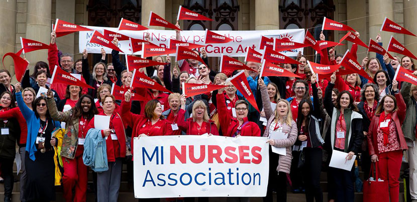 Large crowd of Michigan Nurses Association members posing in red with flags and banner on steps assembled.