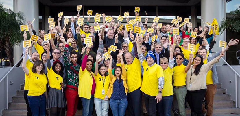 NewsGuild members standing together in yellow, smiling holding signs with arms up