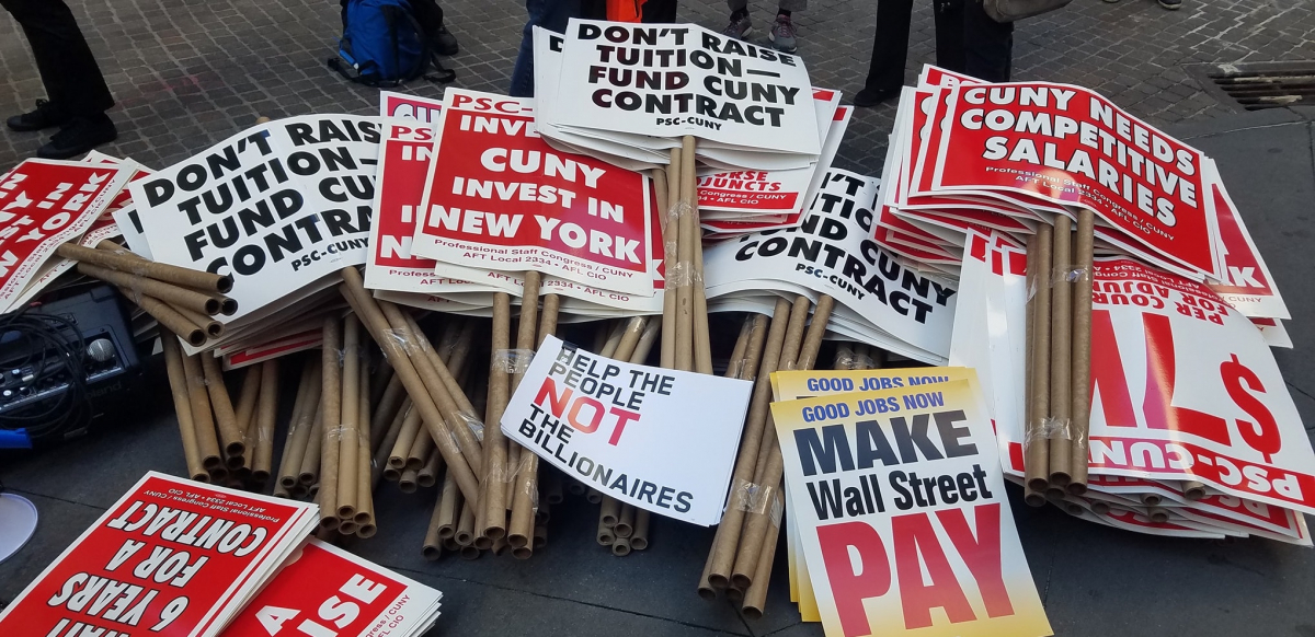 stack of picket signs including "don't raise tuition, fund CUNY contract," "good jobs now, make Wall Street pay," "CUNY invest in New York," "help the people, not the billionaires," and "CUNY needs competitive salaries"