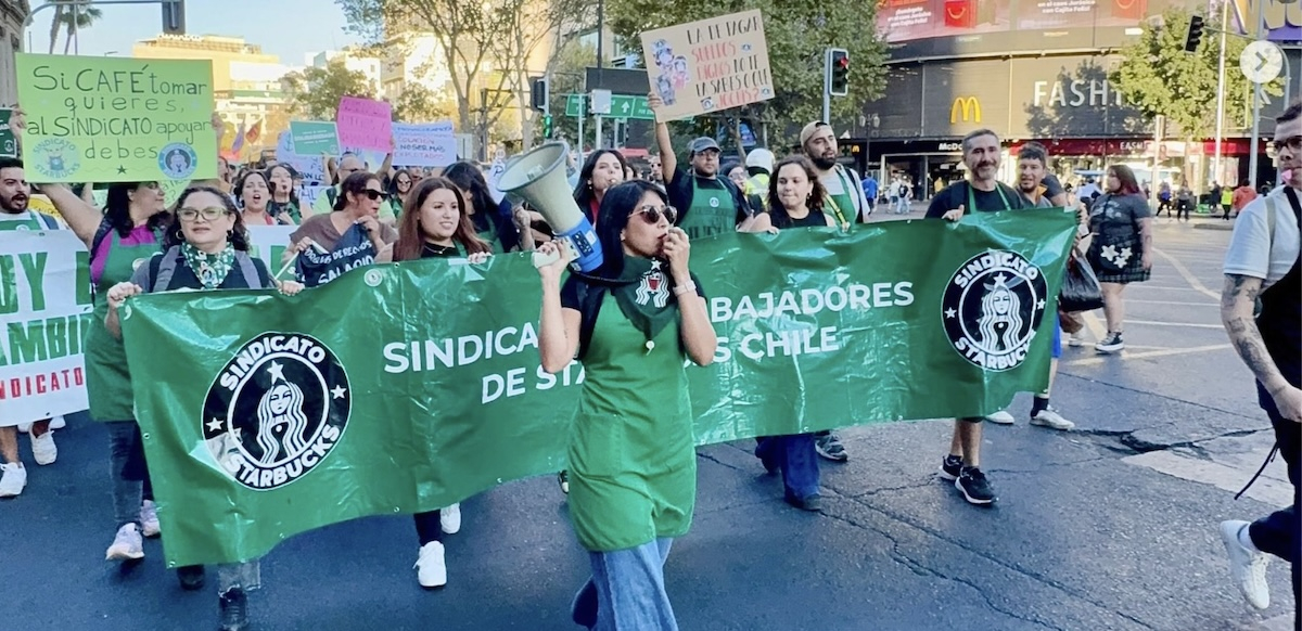 Workers in green aprons march behind a union banner.