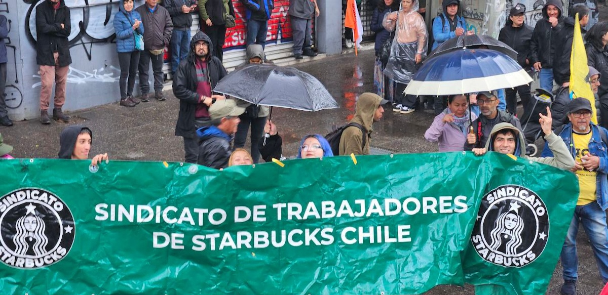Five workers in the rain hold a green banner that says Chilean Starbucks Union in Spanish