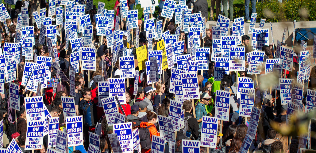 View from above of a sea of marchers outdoors, all carrying matching printed "UAW on strike" picket signs