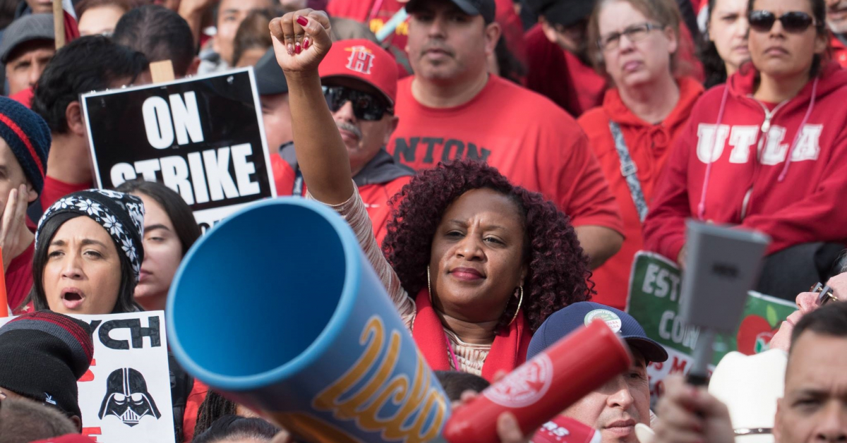 Black woman raising her fist in a crowd of strikers